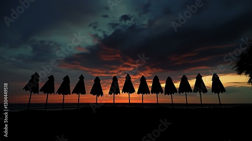 A row of umbrellas lined up on a beach, their dark shapes contrasting with the sunset.