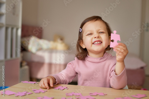 smiling little child girl showing puzzle piece at wooden desk in room