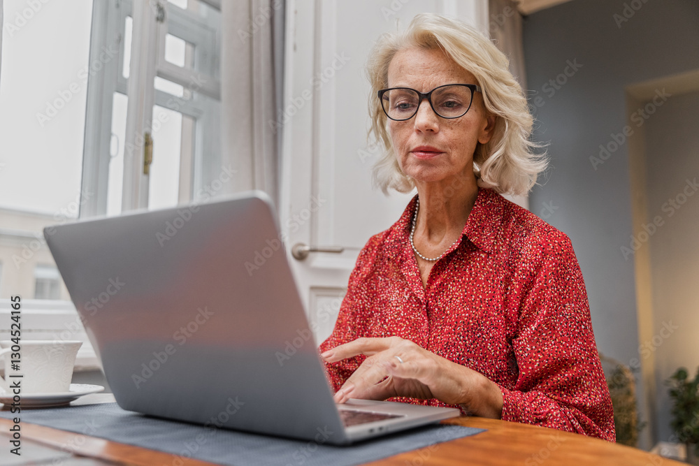 Senior elegant woman sits at table typing on keyboard. Cheerful aged woman working remotely using laptop. Older focused businesswoman browsing online. Female elegant writer enjoying creative process Senior elegant woman sits at table typing on keyboard. Cheerful aged woman working remotely using laptop. Older focused businesswoman browsing online. Female elegant writer enjoying creative process