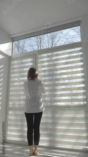 Vertical video of a Woman closing and opening modern room blinds with lighting range control. 4k footage.