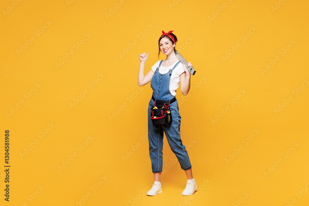 Fototapeta premium Full body young employee laborer handyman woman wears overalls belt hold spirit level show thumb up isolated on plain yellow background. Instruments for renovation apartment room. Repair home concept.