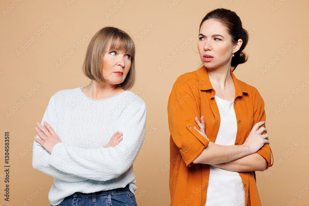 Elder sad mad offended parent mom 50s years old with young adult daughter two women together wear casual clothes hold hands crossed folded isolated on plain light beige background. Family day concept. Elder sad mad offended parent mom 50s years old with young adult daughter two women together wear casual clothes hold hands crossed folded isolated on plain light beige background. Family day concept.