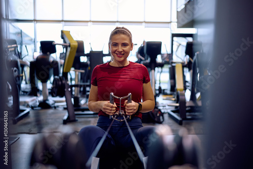Foto Happy athletic woman working out on seated cable row machine in gym and looking at camera