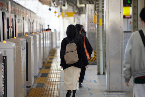 冬の朝の駅のホームで電車待ちの若い女性の姿