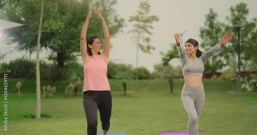Indian happy mature mother teen age girl standing do day time yoga asana raise hands arm pose outdoor garden park young adult two woman lady learn self body health care good habit enjoy outside park Indian happy mature mother teen age girl standing do day time yoga asana raise hands arm pose outdoor garden park young adult two woman lady learn self body health care good habit enjoy outside park