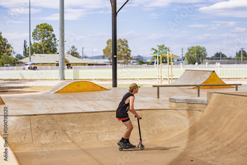 Teen boy riding scooter on ramps at skate park photo