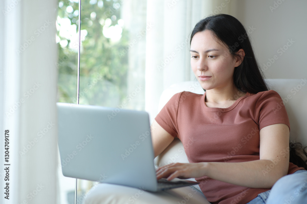 Serous asian woman using laptop on a couch Serous asian woman using laptop on a couch