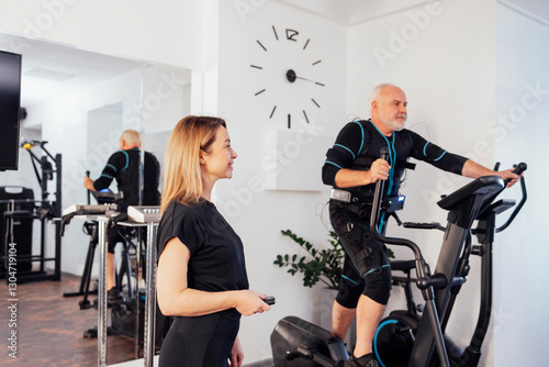 Young smiling trainer is doing electrical muscle stimulation workout for her client.
