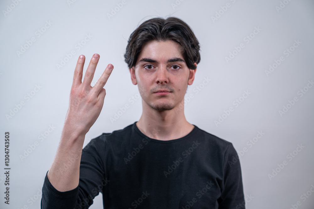 Young man showing 3 fingers and looking at the camera. The man is isolated on white background. The focus is on the hand.