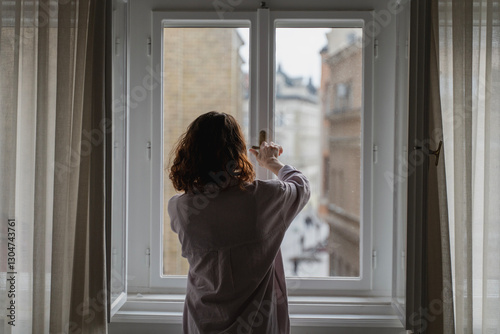 Foto Young woman opens or closes window handle in apartment, back view