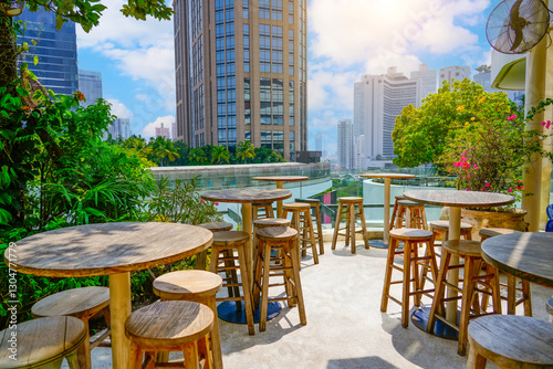 Photography Vibrant outdoor view seating area features rustic wooden tables and stools set against a backdrop of modern skyscrapers under a clear blue sky