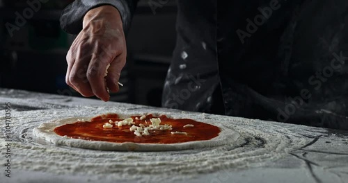Pizza maker makes fresh Italian pizza from a piece of dough. Experienced Chef drop mozzarella cheese on tomato sauce pizza. Pizzaiolo making food in bakery. Pizzeria restaurant making handmade pizza.