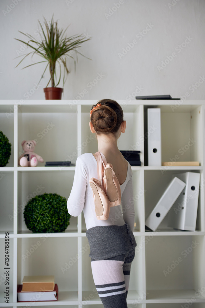 Young ballet student with pointe shoes over shoulder, standing in a modern studio interior