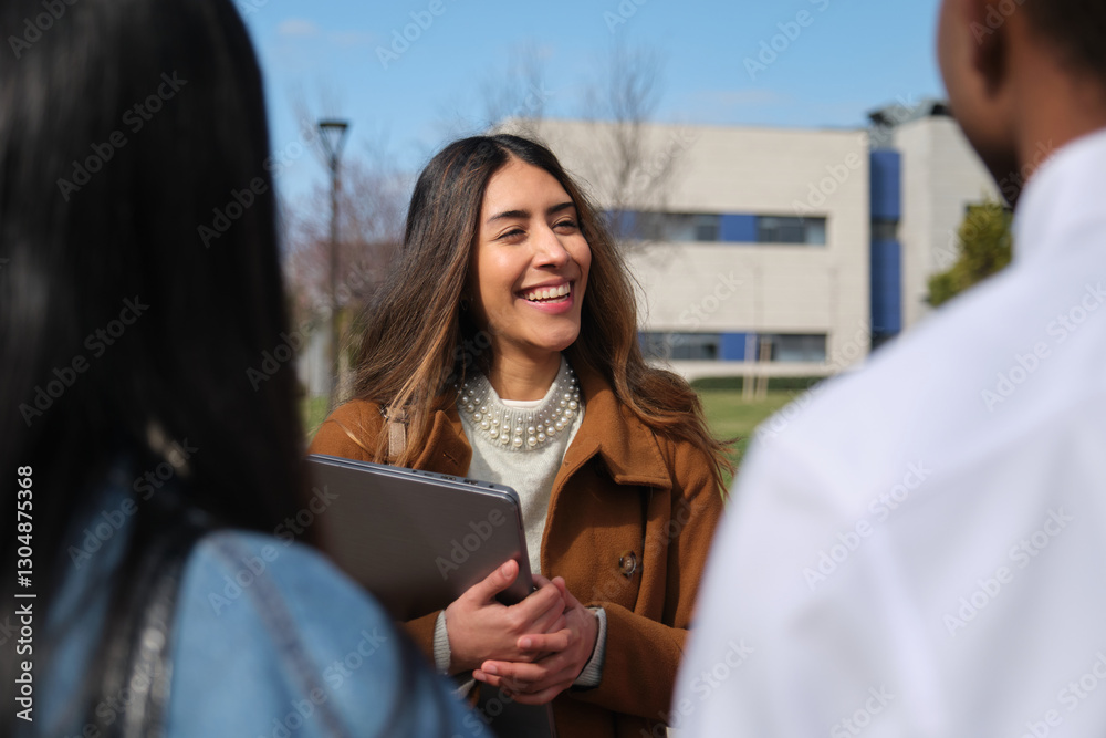 Young woman holding laptop is happily talking with colleagues in university campus