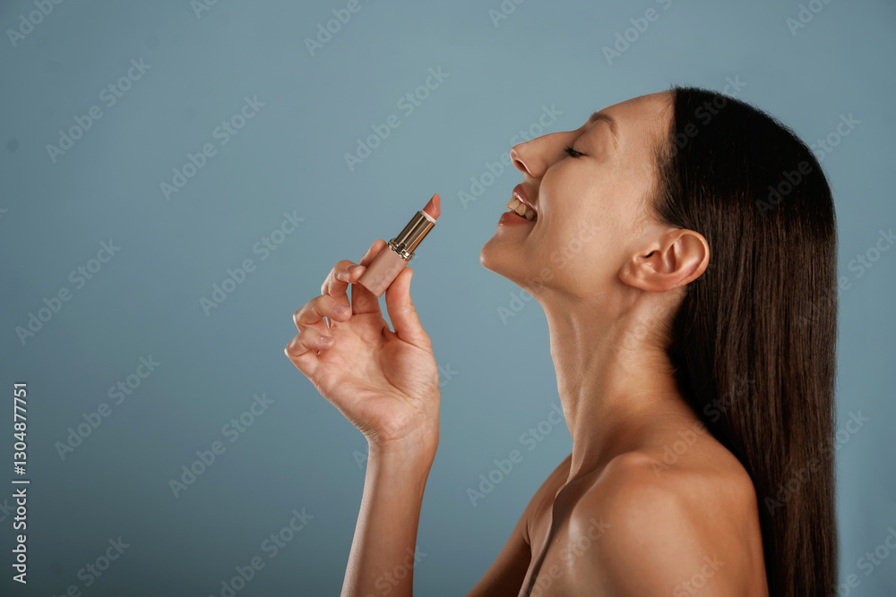 Obraz premium Applying lipstick. Young woman is in the studio against background