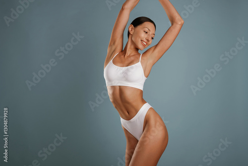 Fitness model is in white underwear. Young woman is in the studio against background