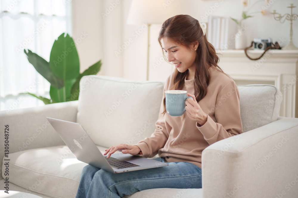 Asian woman sits comfortably on a couch, using her laptop while holding a mug. Asian woman sits comfortably on a couch, using her laptop while holding a mug.