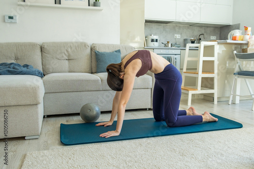 Woman performing a cat-cow yoga stretch on a mat at home, flexibility exercise
