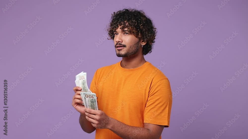 Happy accountant young Indian man he wear orange t-shirt casual clothes hold in hand count stack of cash money in dollar banknotes isolated on plain pastel light purple background. Lifestyle concept Happy accountant young Indian man he wear orange t-shirt casual clothes hold in hand count stack of cash money in dollar banknotes isolated on plain pastel light purple background. Lifestyle concept