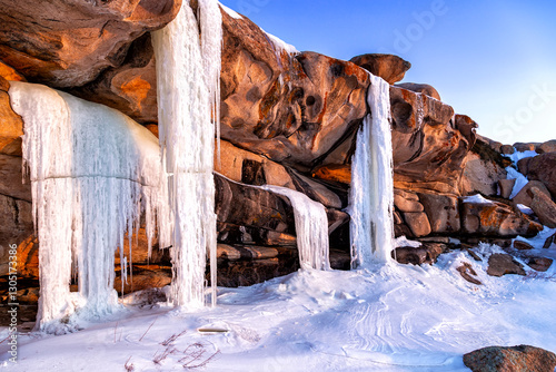 Bektau Ata, Kazakhstan. Frozen waterfall with large icicles in spring at dawn in the sun with water droplets among huge granite rocks with bizarre shapes
