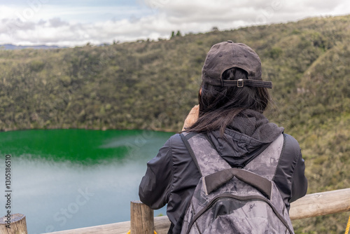 Woman photographer with big backpack taking photo with cellphone of mountains and blue lake. Travel and hobby concept