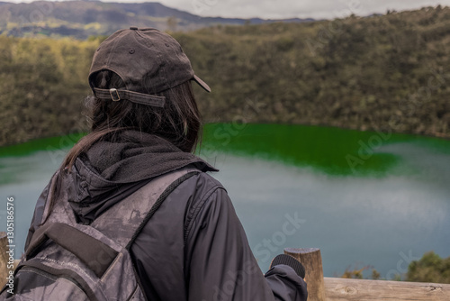 Woman photographer with big backpack taking photo with cellphone of mountains and blue lake. Travel and hobby concept