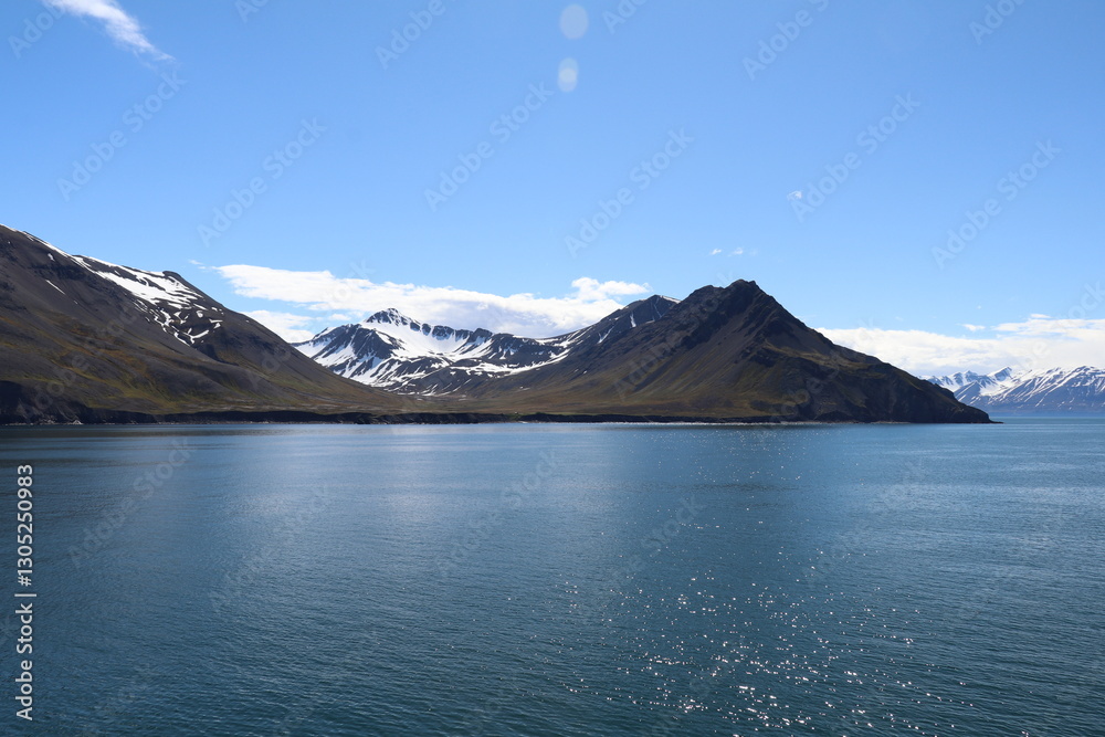 tranquil scenery of an Icelandic fjord with calm waters, blue sky and snow capped mountains on the horizon tranquil scenery of an Icelandic fjord with calm waters, blue sky and snow capped mountains on the horizon