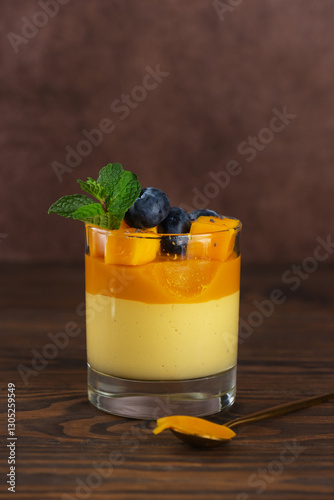Vegan mango panna cotta mousse pudding with blueberries and mint leaf on a wooden table. Sugar, lactose and sugar substitutes free. Vertical orientation.