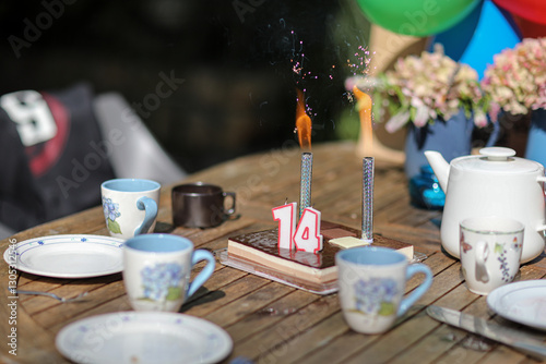 Summer garden birthday party with balloons, cake, and lit candles. Festive atmosphere outdoors with colorful decorations and joyful celebration under sunny skies.