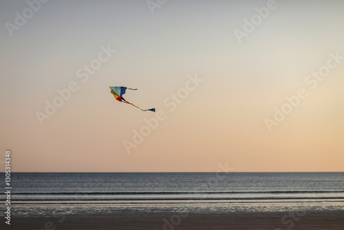 Silhouette of  flying a kite at the beach during sunset. Warm evening light, calm sea, and joyful holiday mood create a peaceful and nostalgic summer scene.