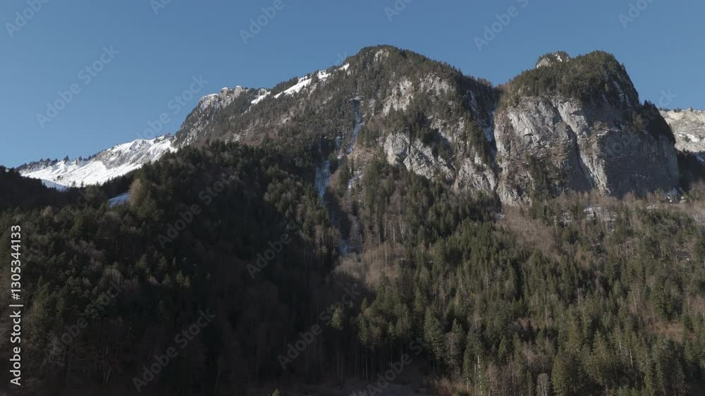 Snowy mountain peaks under a clear blue sky, overlooking a valley with scattered houses. An idyllic Alpine panorama perfect for travel, nature, and landscape photography.