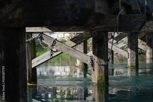 Metal chain tied to a wooden bridge pillars, this structure is built to cross the Livenza river in Polcenigo, close to the Santissima location (Friuli Venezia Giulia)