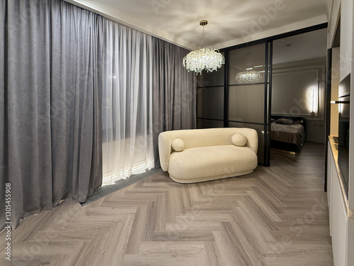 A contemporary living area features a plush, rounded sofa with stunning chandelier lighting. The muted color scheme and sleek lines create an inviting atmosphere.