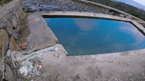 A natural hot spring pool with crystal-clear thermal water, surrounded by stone structures and overlooking the sea. A peaceful and scenic outdoor spa experience in a remote location, perfect for relax