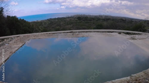 A natural hot spring pool with crystal-clear thermal water, surrounded by stone structures and overlooking the sea. A peaceful and scenic outdoor spa experience in a remote location, perfect for relax