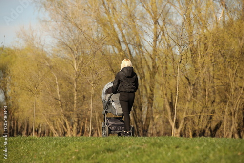 A young mother walks in the park with a baby carriage on a sunny day. Baby's stay in the fresh air. Raising the younger generation. Guardianship of human offspring.