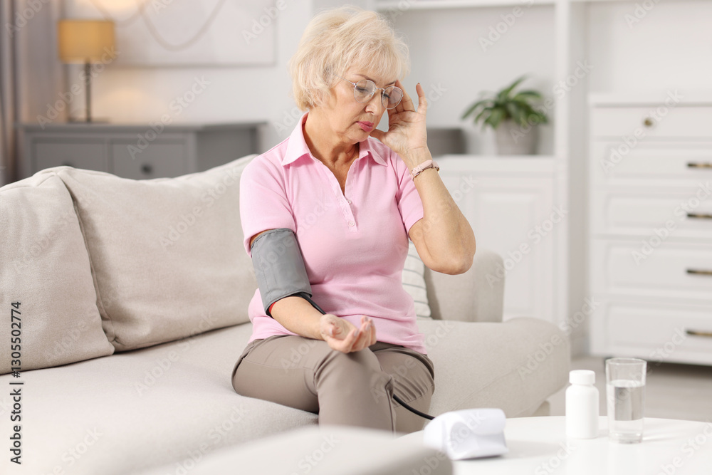 Senior woman measuring blood pressure on sofa at home Senior woman measuring blood pressure on sofa at home