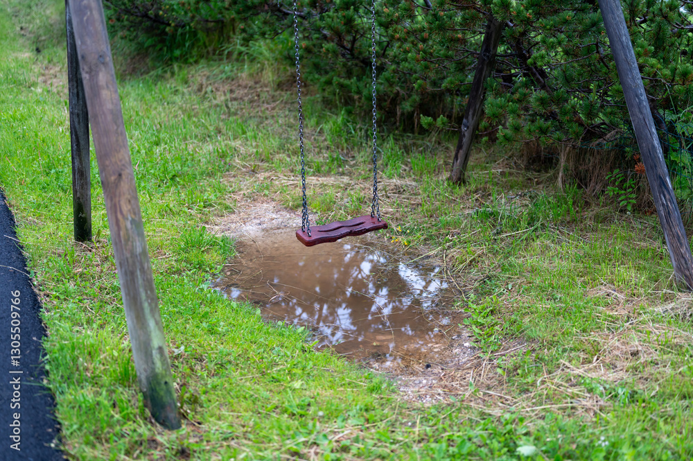 A wooden swing suspended above a water puddle, reflecting the serene atmosphere of nature. A peaceful and nostalgic scene that invites relaxation and contemplation