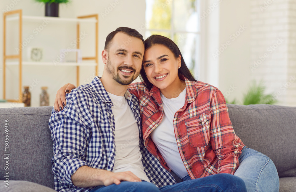 Portrait of young happy married couple sitting on the sofa in the living room at home. Smiling family man and woman on the couch hugging and looking at camera. Harmonic relationships concept. Portrait of young happy married couple sitting on the sofa in the living room at home. Smiling family man and woman on the couch hugging and looking at camera. Harmonic relationships concept.