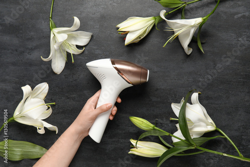 Female hand with modern photoepilator and beautiful lily flowers on grunge black background photo