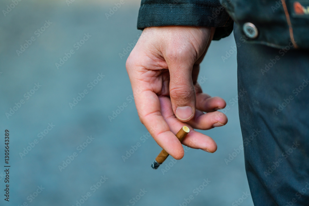 Fototapeta premium Man smoking a cigar type of brown cigarette in a construction yard close up of arm holding the cigarette