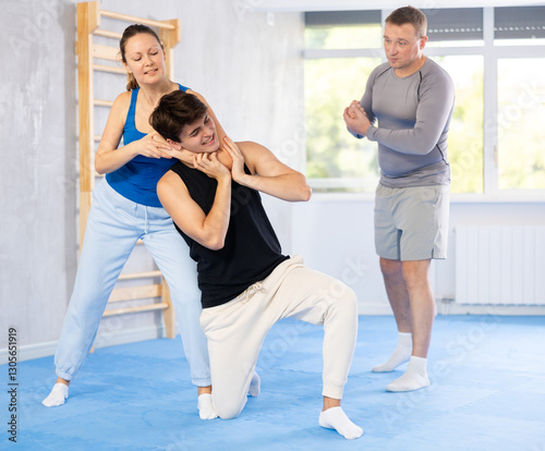 Guy and woman paired up and practice technique of strangulation to neutralize opponent and attacker. Class self-defense training in presence of experienced instructor