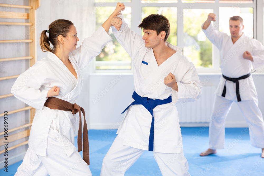 Fototapeta premium Woman and man in pairs exercising karate movements during group training