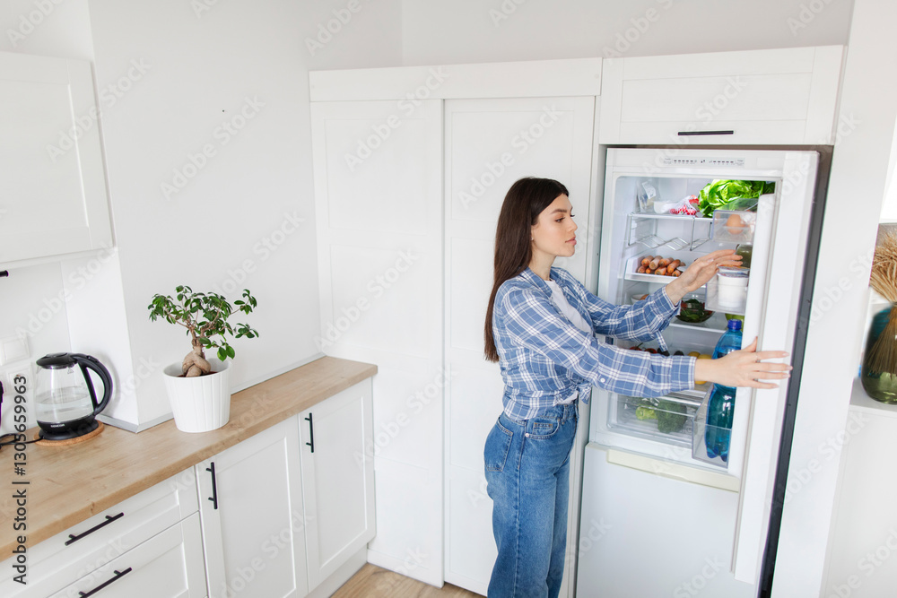 Above view of young lady taking out products from refrigerator, planning what to cook at home, kitchen interior, free space