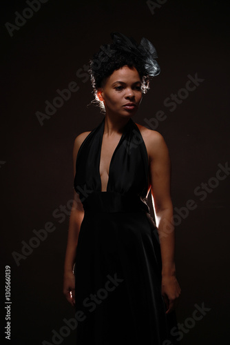 Low key portrait of pretty curly woman in black dress with back light