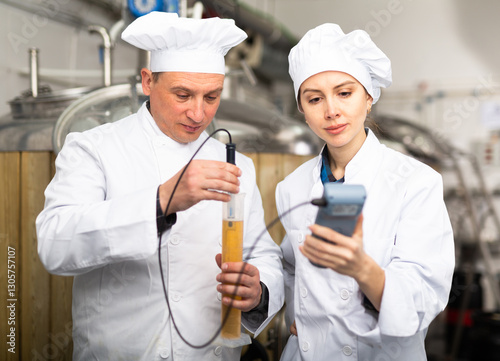 Man and woman brewmasters measuring strengh of beer sample with alcoholometer.