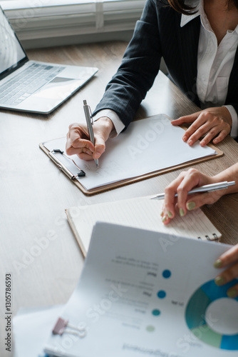 Professionals reviewing financial documents and taking notes during a business meeting in a modern office environment.