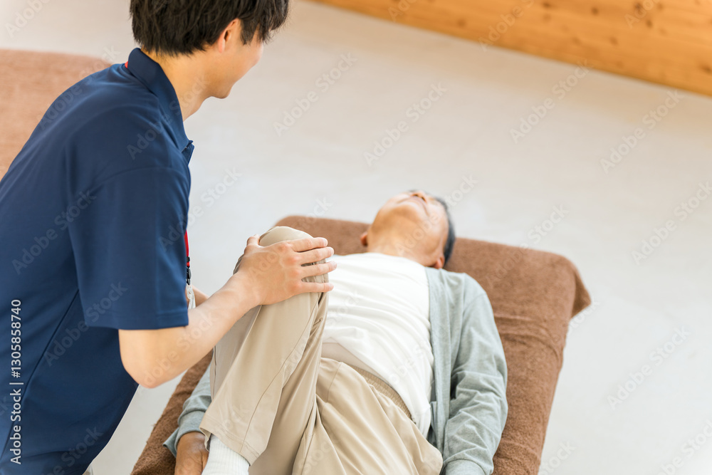 Fototapeta premium リハビリでマッサージ・ストレッチをするシニア男性と理学療法士・作業療法士の男性スタッフ