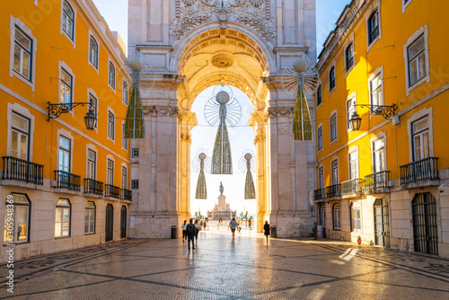 Fotografie Pedestrians walk on the decorated Portuguese Pavement calçada near the historic Arco da Rua Agusta arch on Praça do Comércio square in the Baixa city center district of Lisbon, Portugal