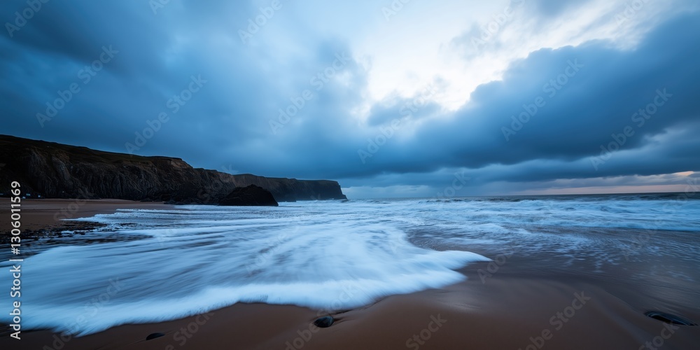 Obraz premium Dramatic sea waves crash onto a stormy beach, with imposing cliffs in the background setting a striking contrast against the turbulent sky.